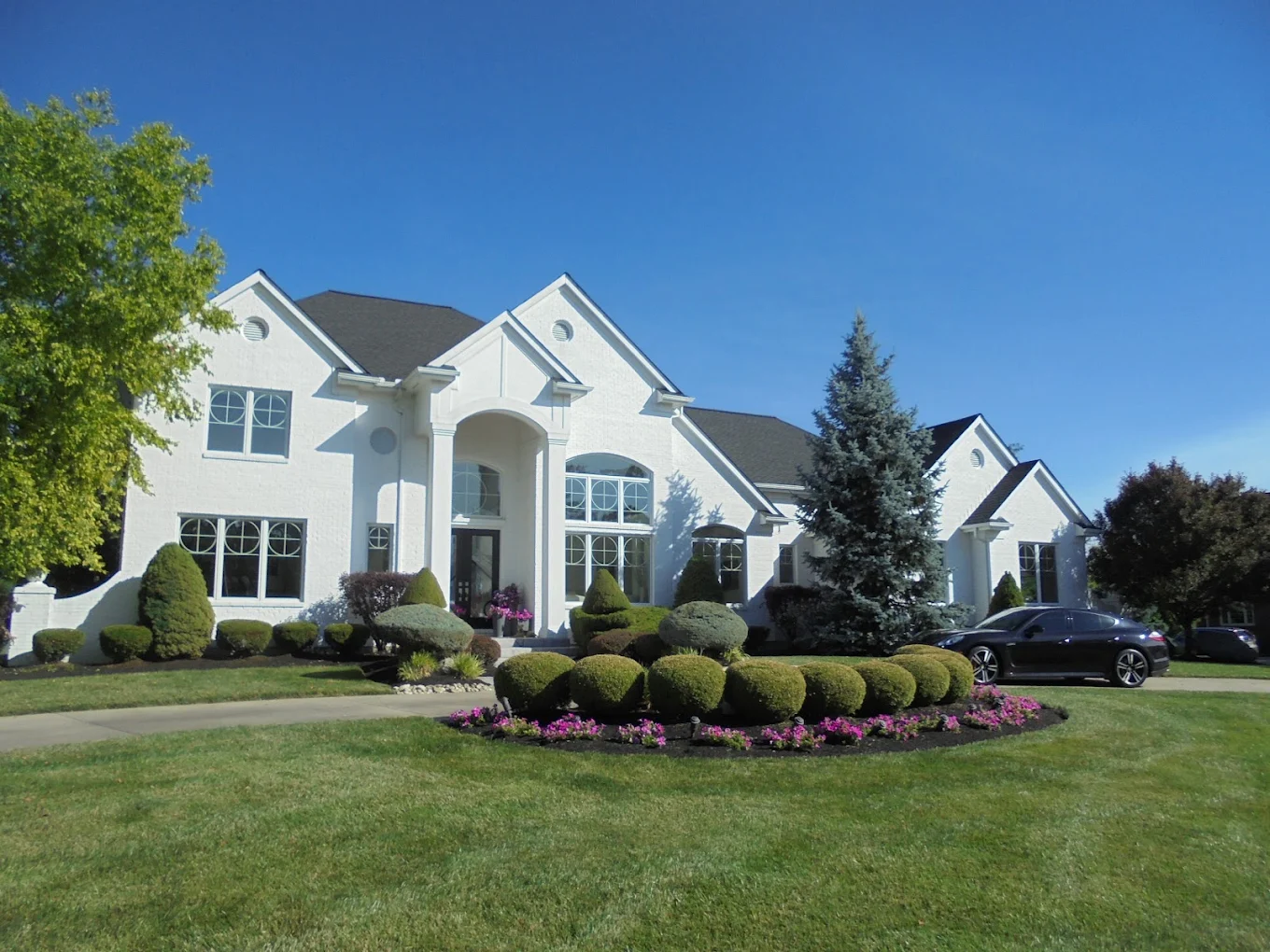 A stately white brick home with manicured landscaping under a clear blue sky